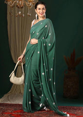 Woman in a green saree with white patterns holding a beige handbag against a dark background.