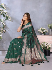 Woman in a green saree with silver embroidery sitting against a gray background with floral decorations.