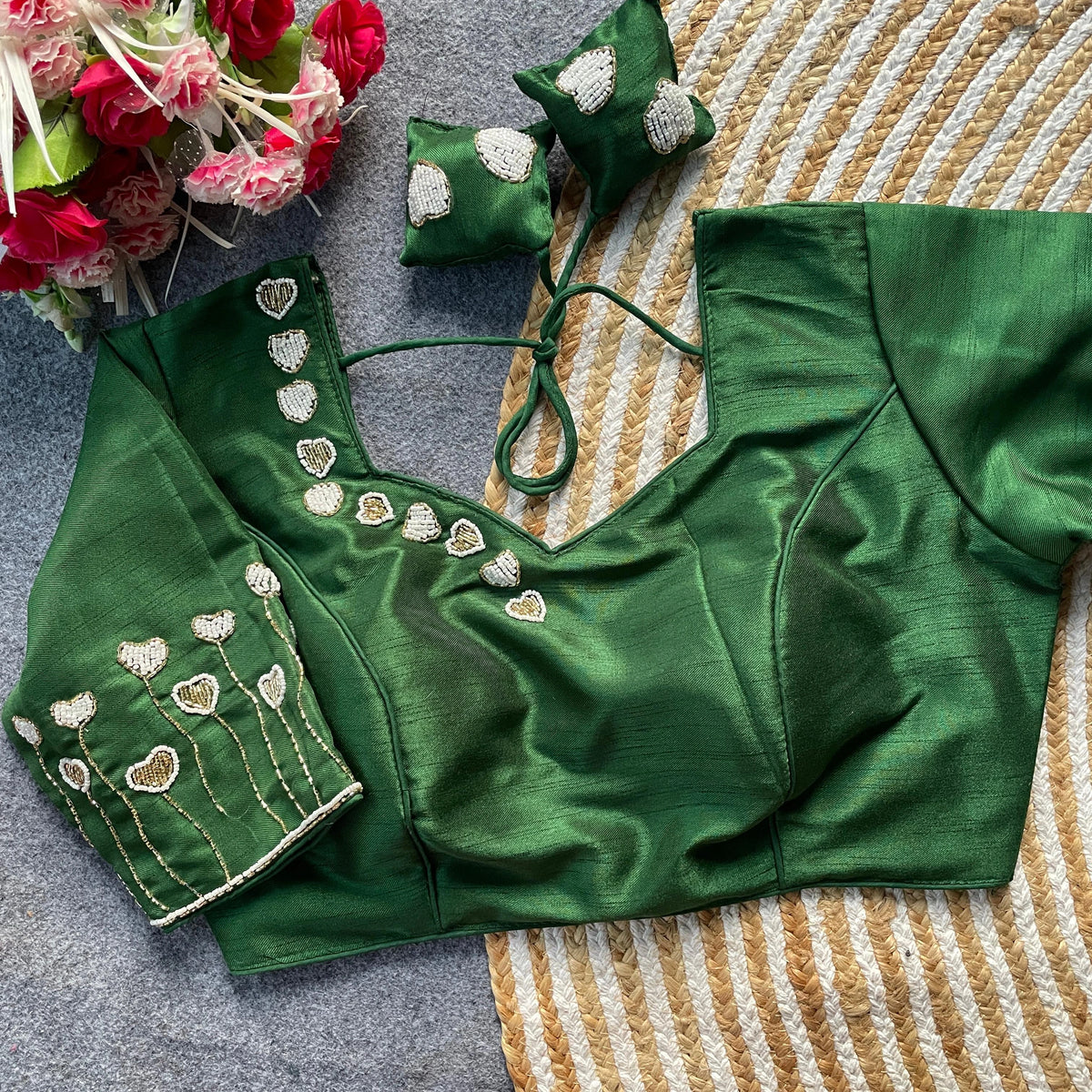 Green blouse with floral embroidery on a textured surface with flowers in the corner