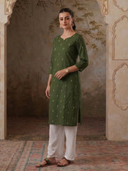 Woman wearing a green kurta with white pants in an ornate room.