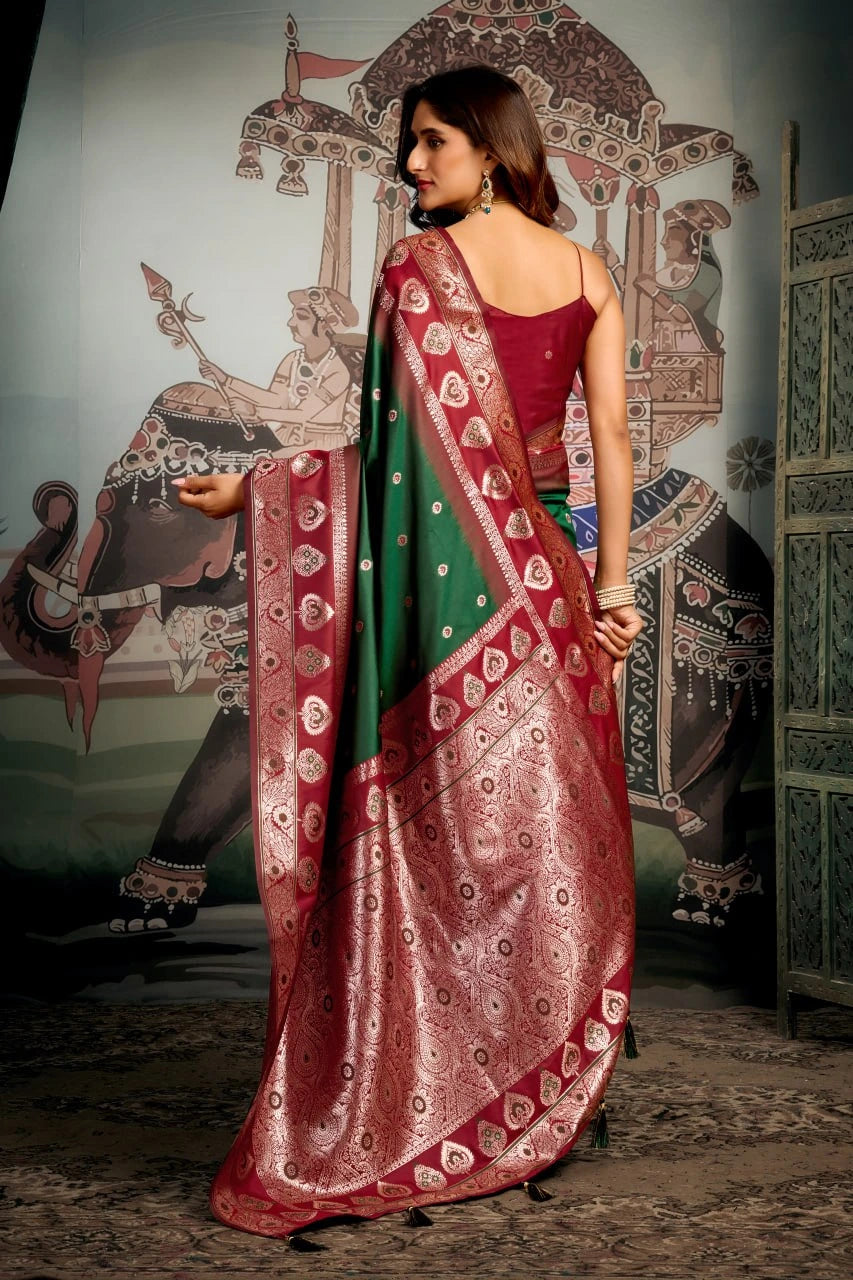 Woman in a red and green saree standing in front of an ornate wall mural.