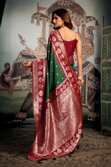 Woman in a red and green saree standing in front of an ornate wall mural.