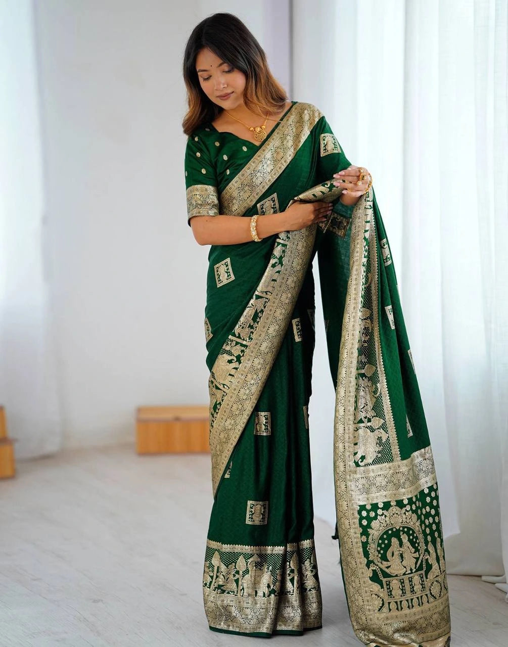Woman holding a green saree with gold patterns in a minimalistic setting
