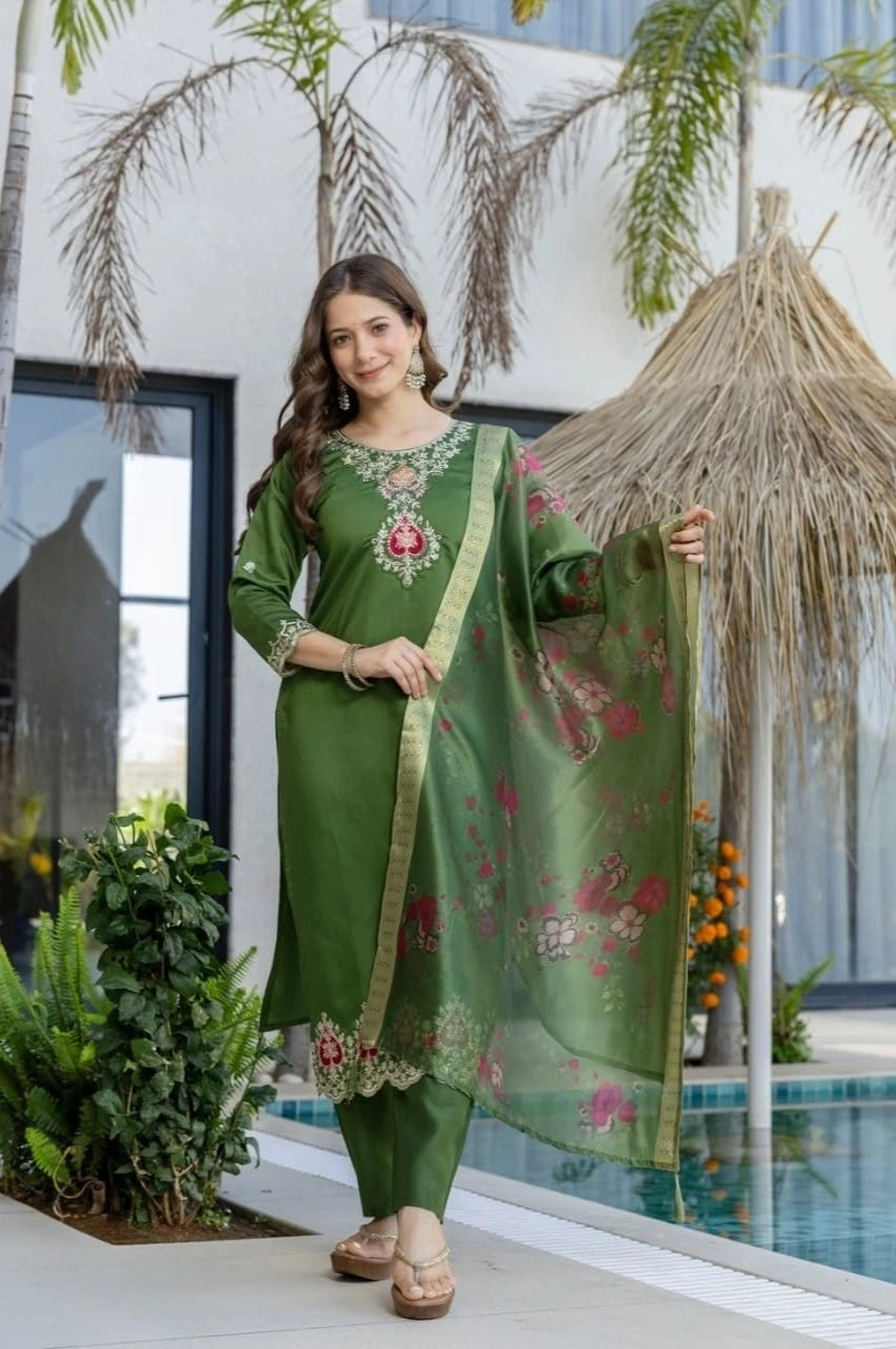 Woman in a green traditional outfit standing by a poolside with plants and umbrellas in the background.
