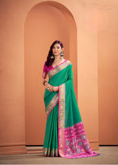 Woman wearing a green and pink saree with a beige wall background