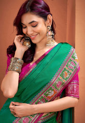 Woman wearing a green and pink saree with jewelry against a brown background