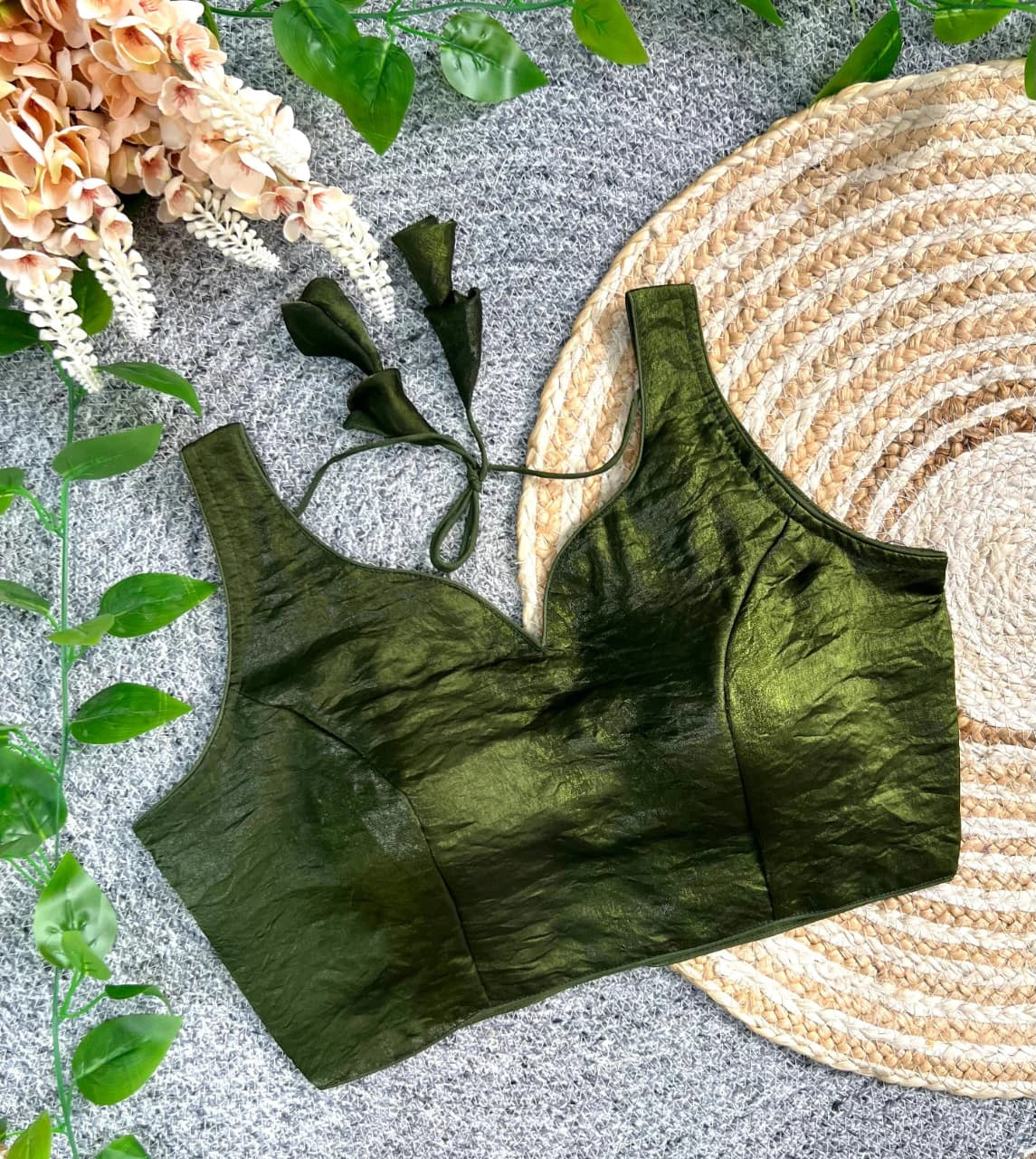 Green satin bralette on a textured surface with floral and woven mat elements.