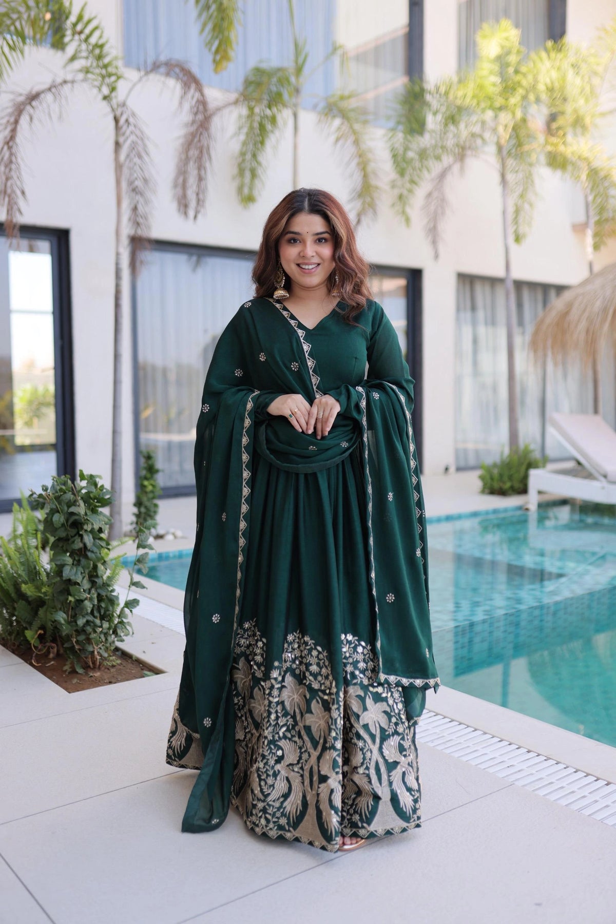 Woman in a green traditional outfit standing by a pool with a modern building in the background
