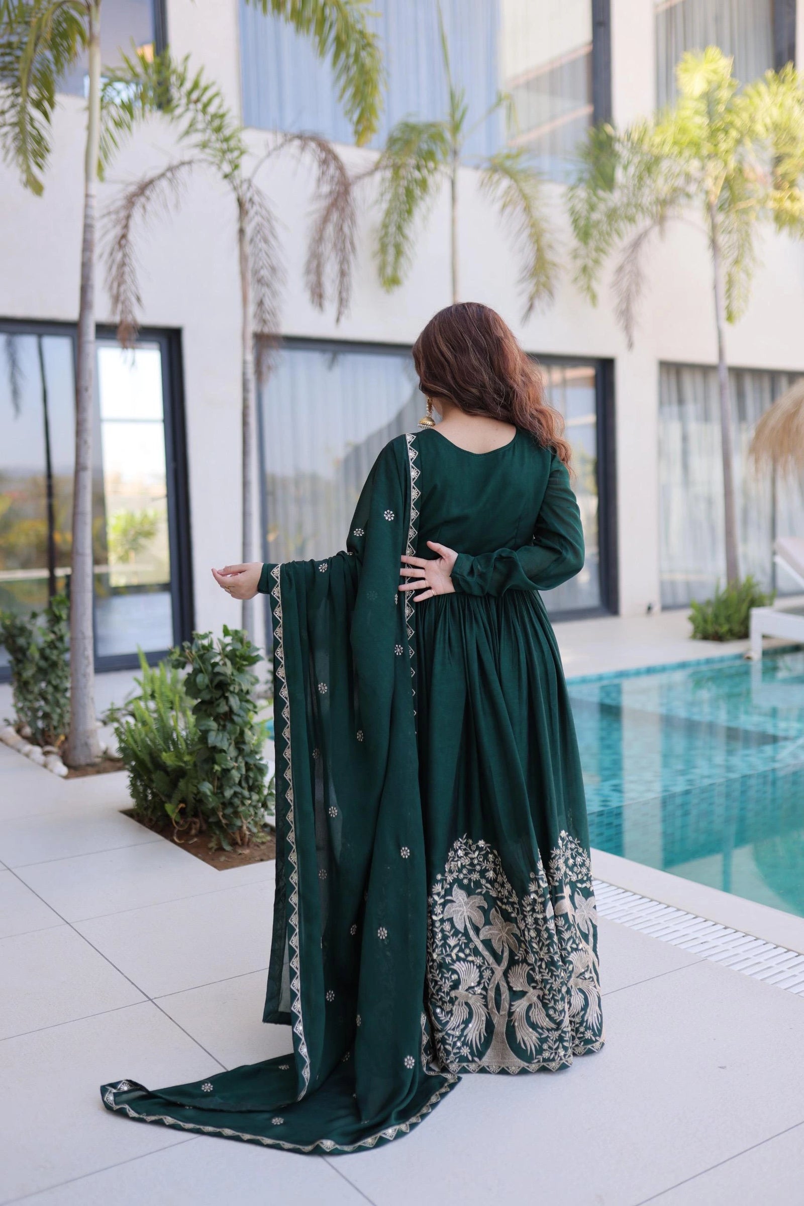 Woman in a green dress standing by a pool with modern building and palm trees in the background
