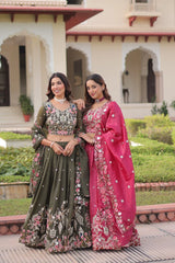 Two women in traditional outfits standing outdoors with a building and garden in the background.