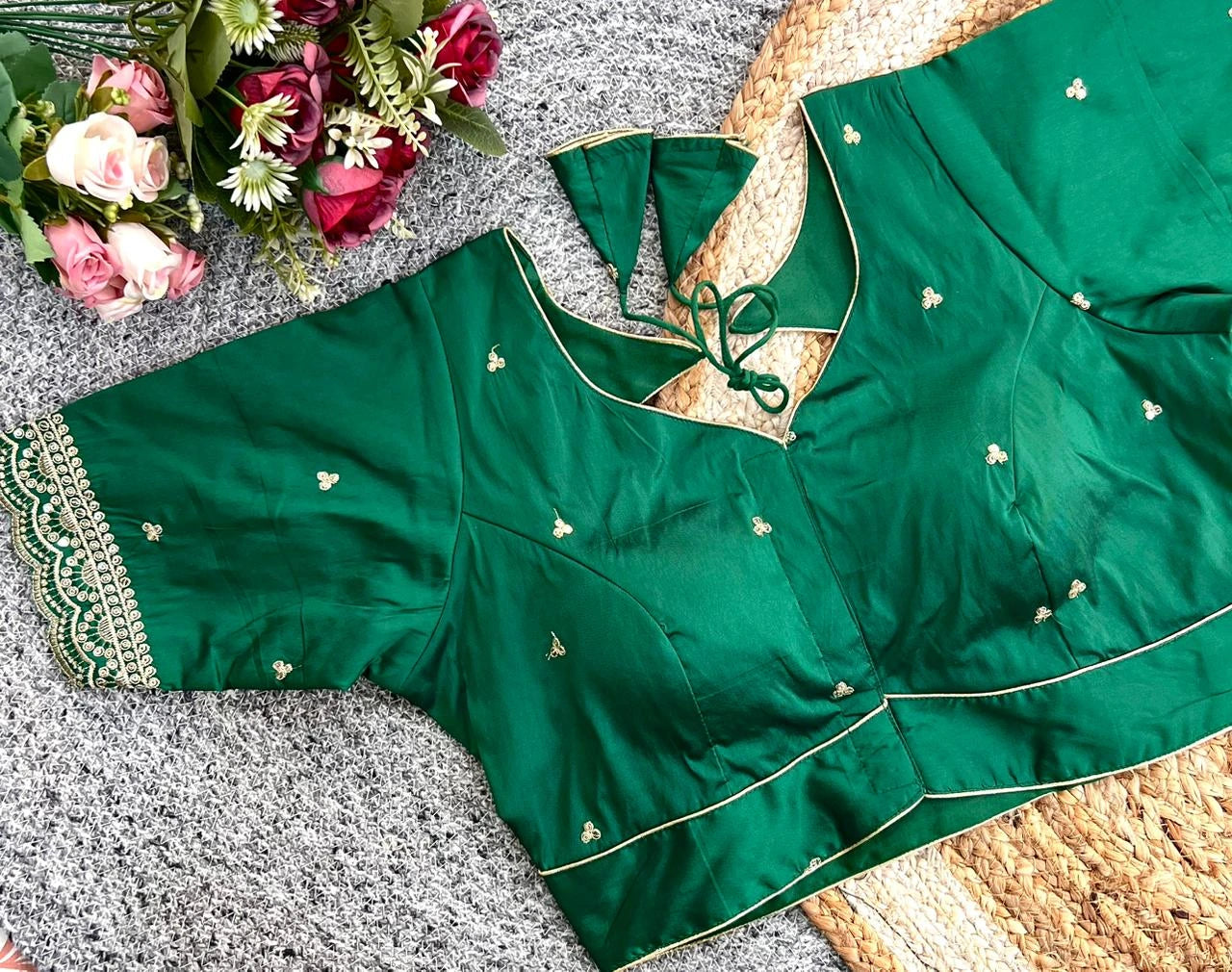 Green saree with intricate embroidery on a textured surface with flowers.