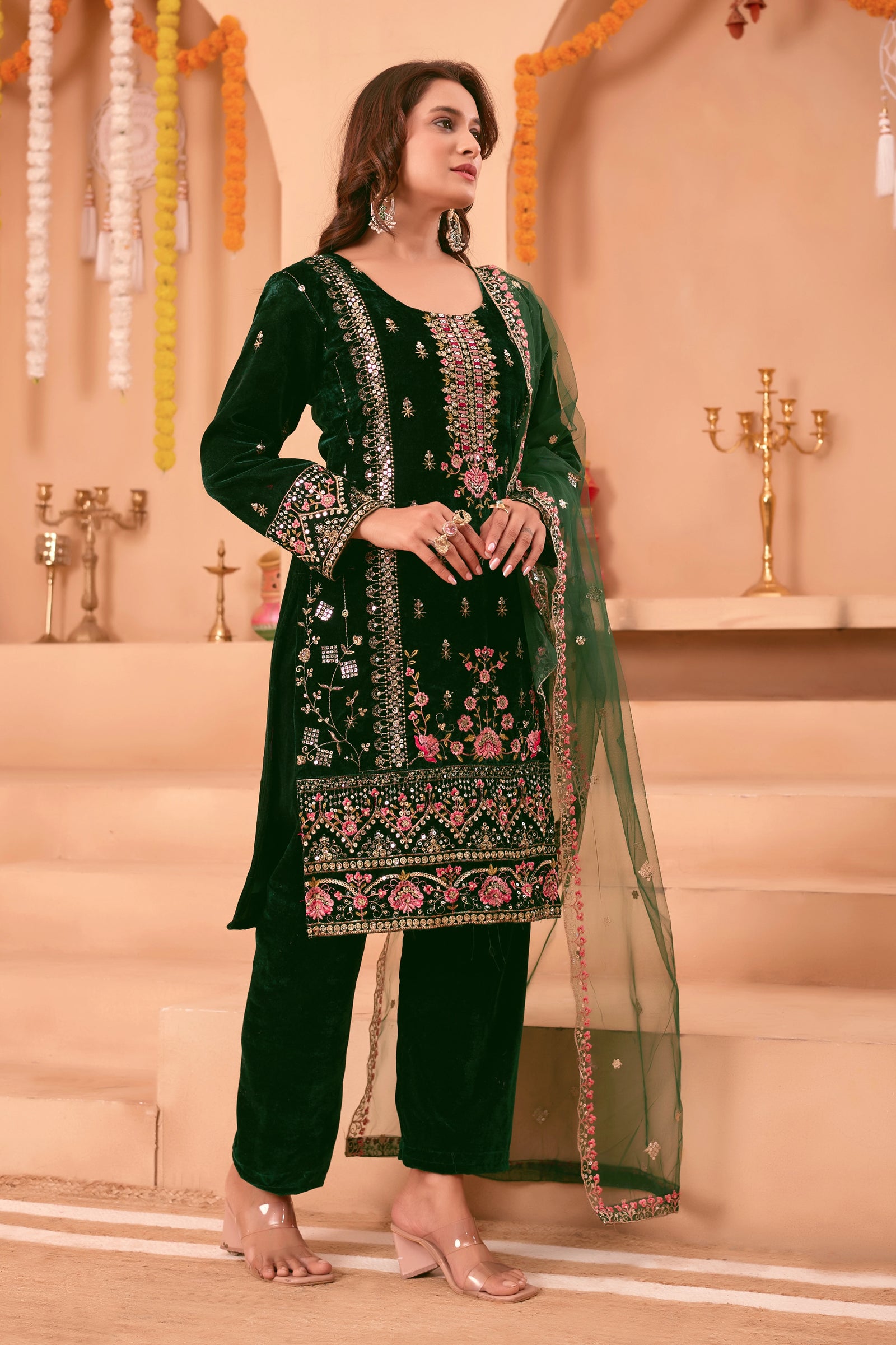 Woman wearing a green embroidered traditional outfit in a decorated indoor setting.