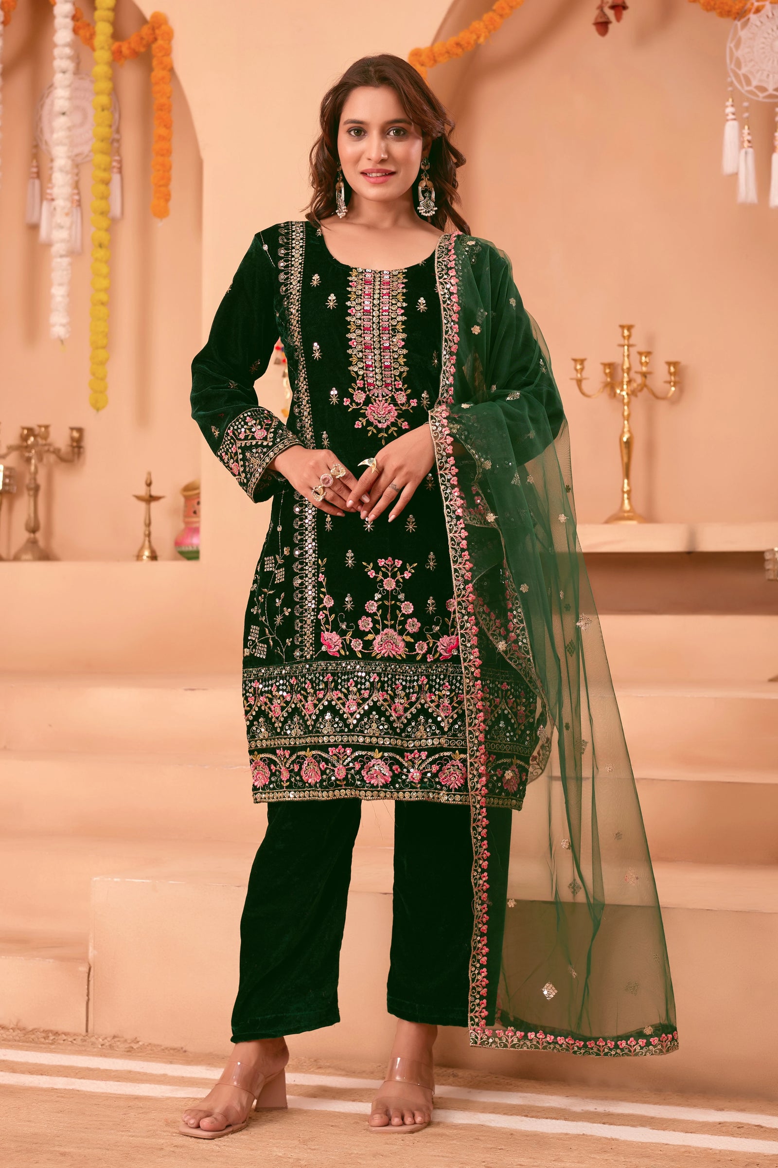 Woman in a green embroidered traditional outfit standing in front of a decorated background.