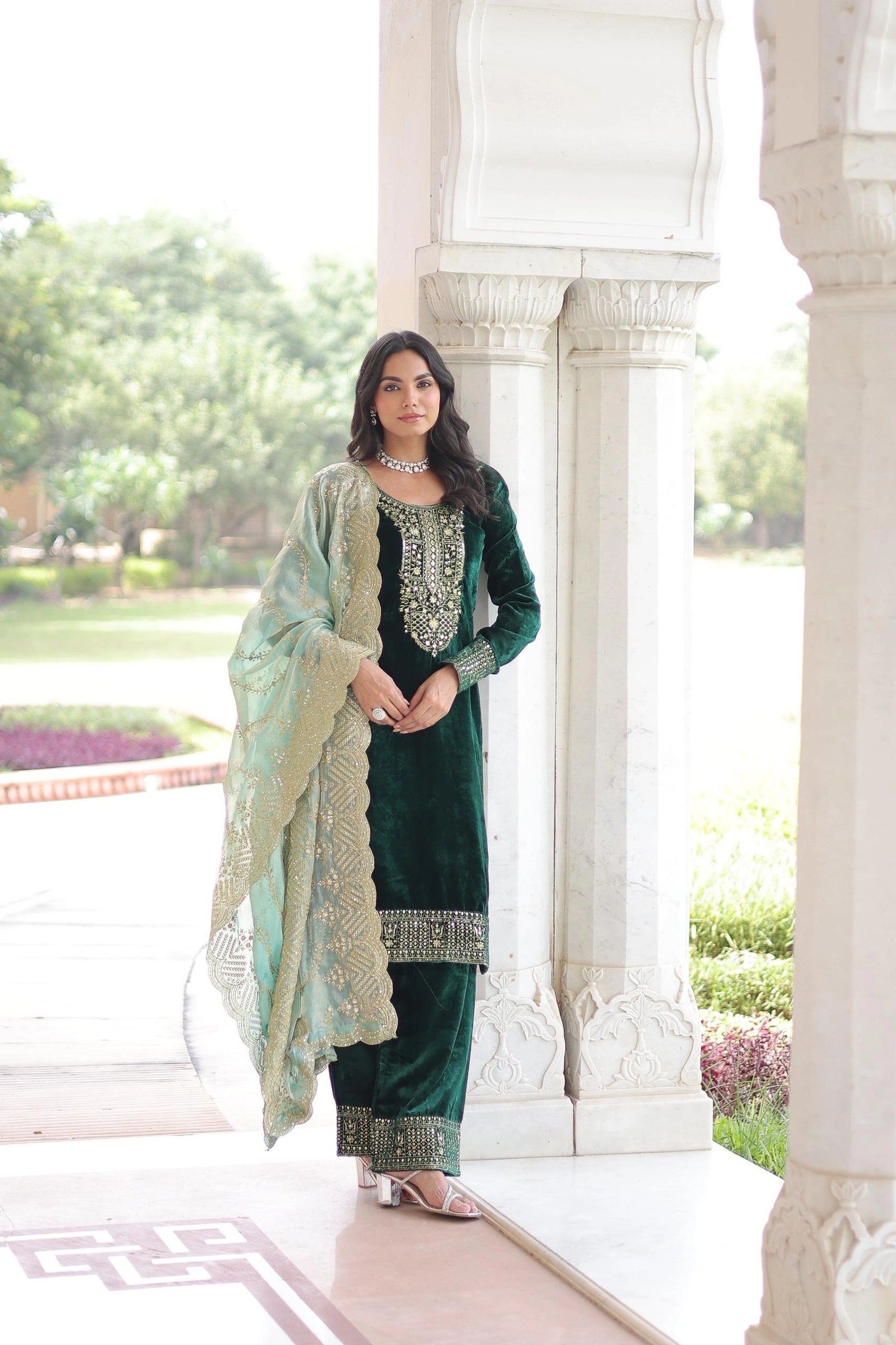 Elegant navy blue velvet suit with intricate gold embroidery, paired with a sheer embellished dupatta, styled in a classic architectural setting.