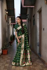 Woman in a green saree with floral patterns standing in a narrow alleyway.