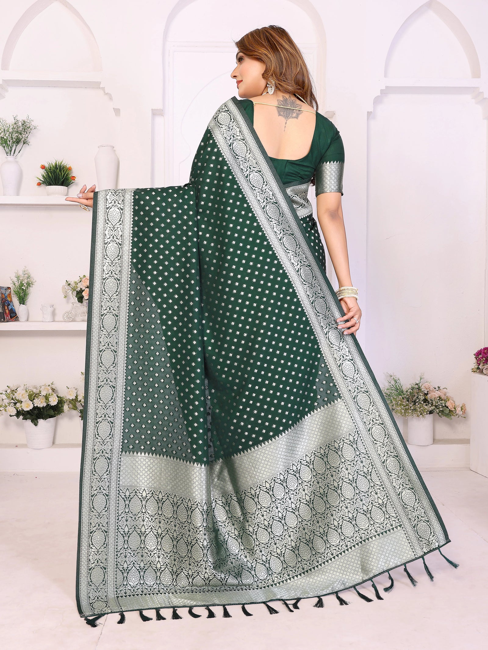 Woman holding a green saree with white patterns in a white room.