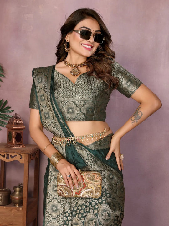 Woman in a green saree with a matching blouse, posing against a purple background.