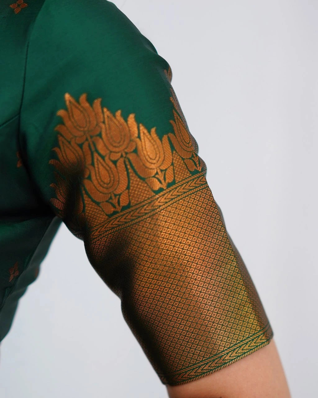 Close-up of a green garment with intricate gold embroidery on a white background
