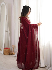Woman in a burgundy dress with pearl embellishments standing in a bright room.