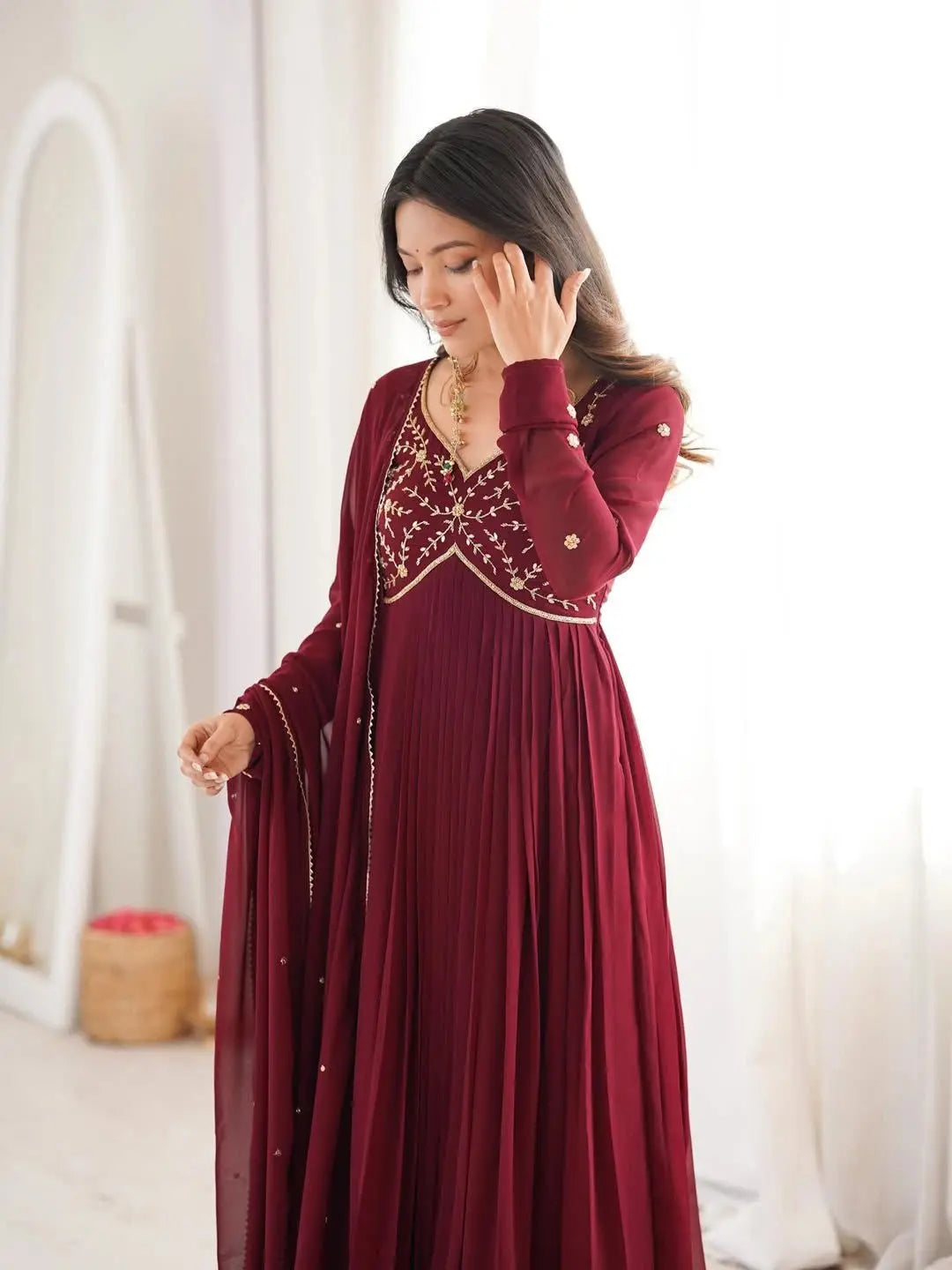 Woman wearing a burgundy dress with intricate detailing in a bright room.