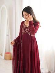 Woman wearing a burgundy dress with intricate detailing in a bright room.