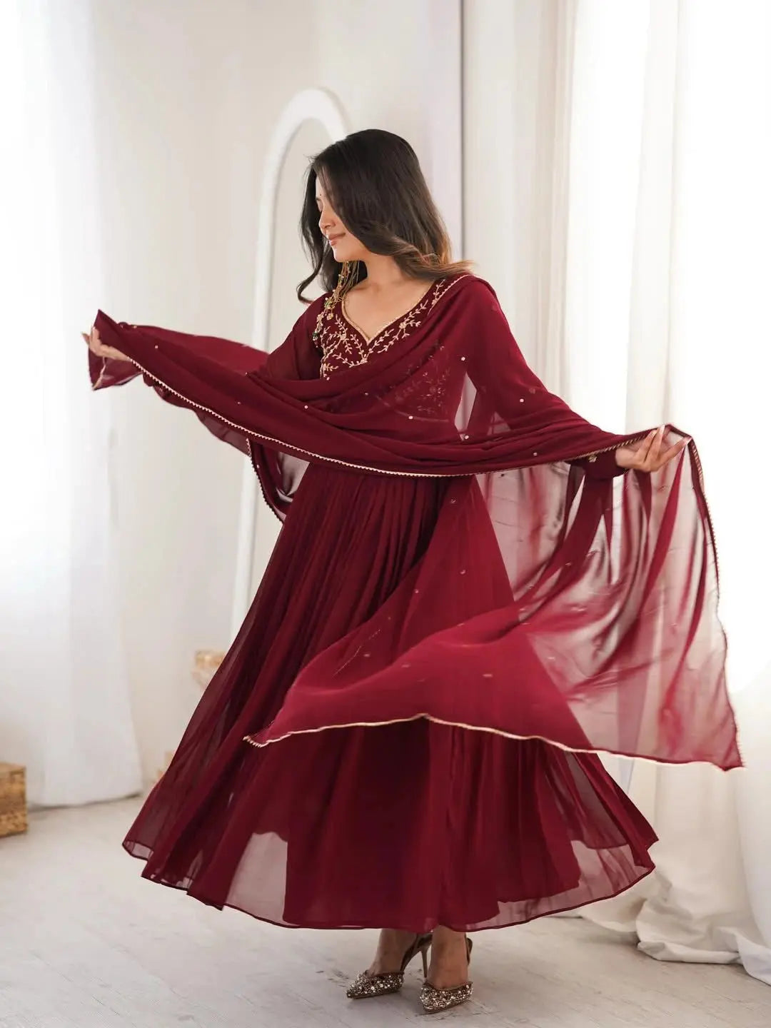 Woman wearing a burgundy traditional outfit with a long scarf in a bright room.