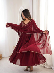 Woman wearing a burgundy traditional outfit with a long scarf in a bright room.