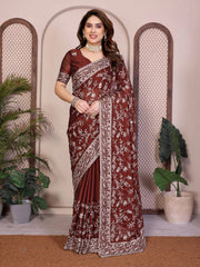 Woman wearing a maroon saree with white patterns in a decorative setting with plants.