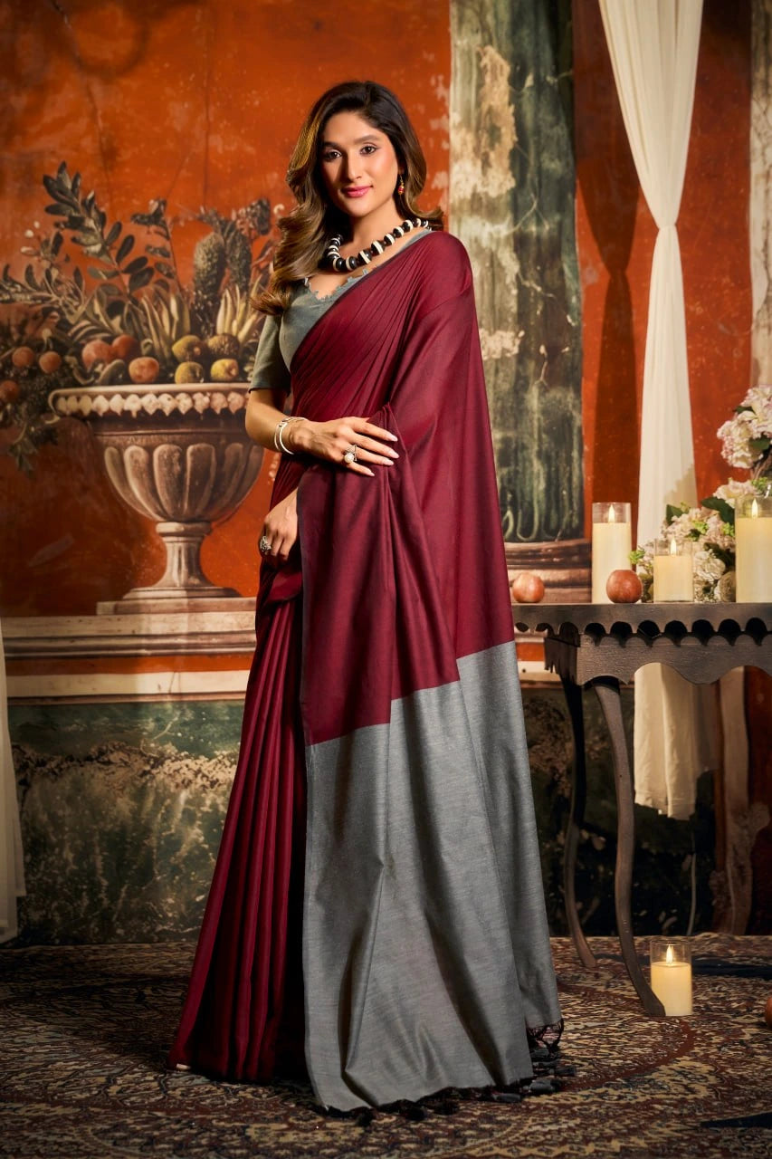 Woman wearing a maroon and gray saree in an elegant room with decorative elements.