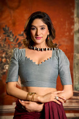 Woman wearing a gray blouse with a red saree against an orange wall.