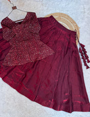 Maroon traditional outfit with a patterned top and pleated skirt on a textured surface