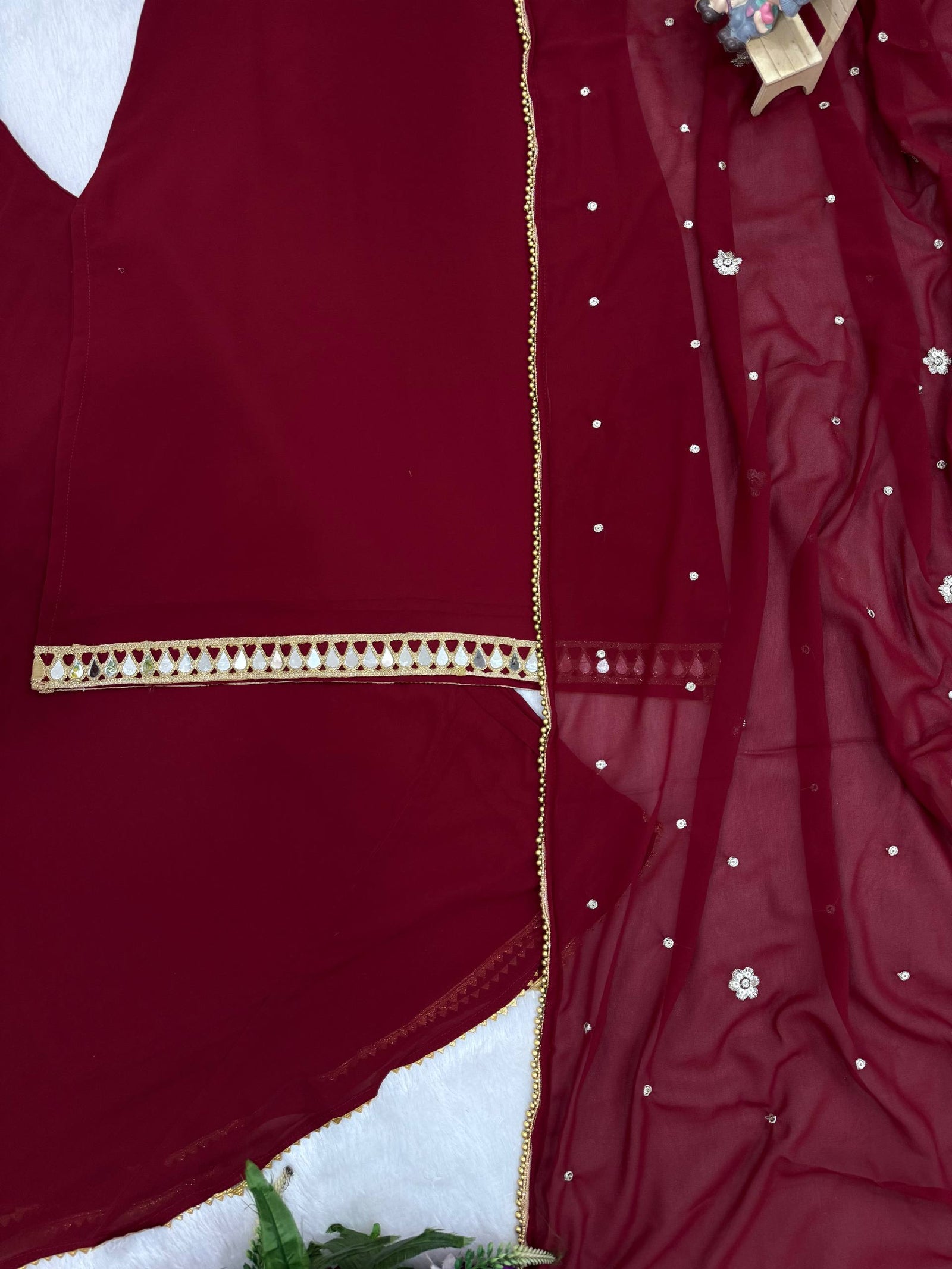 Maroon fabric with gold trim and pearl embellishments on a white background
