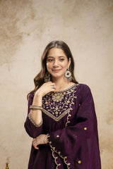 Woman wearing a purple embroidered outfit with gold details against a beige background