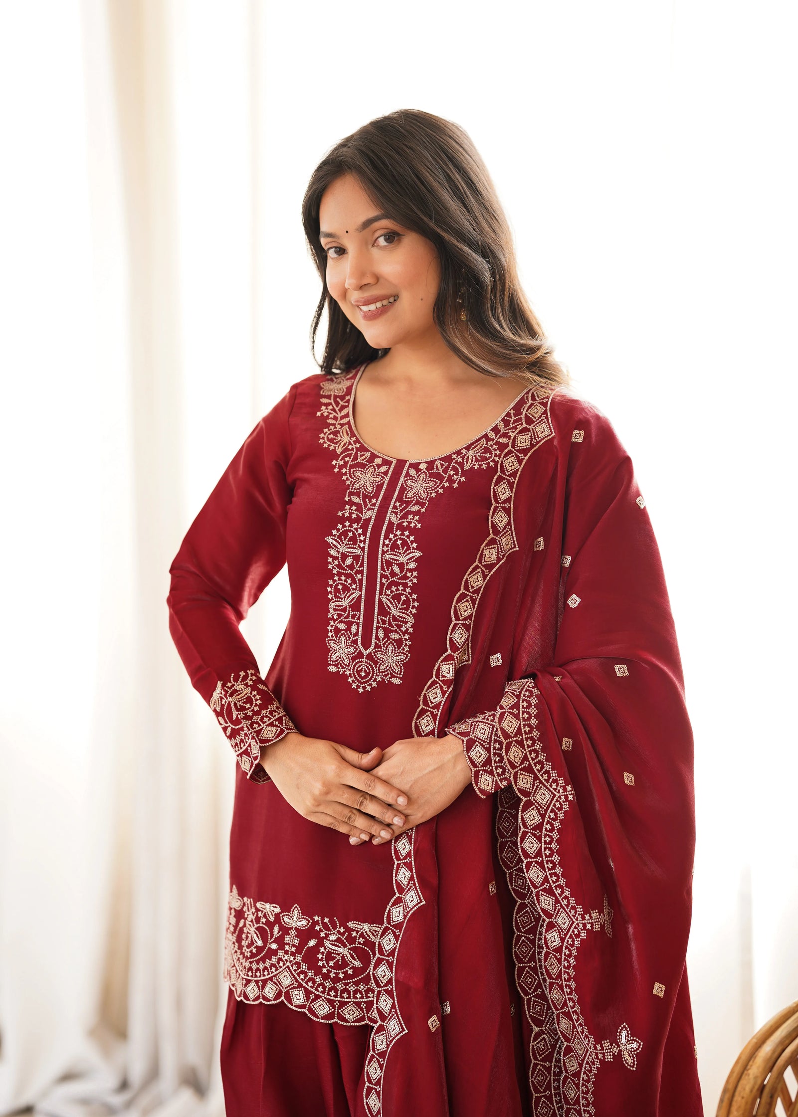 Woman wearing a red traditional outfit with white embroidery against a neutral background