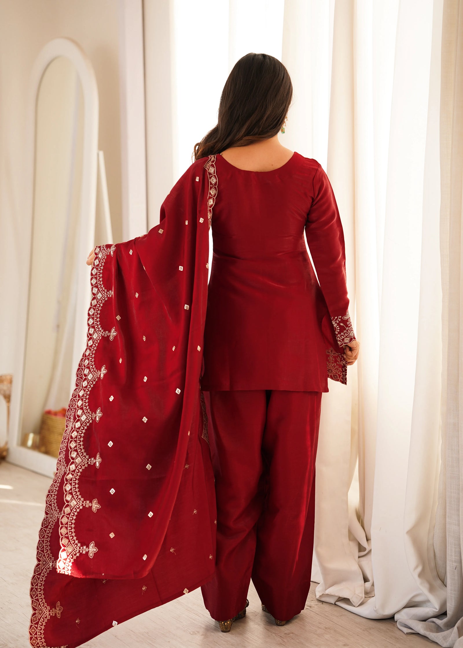 Woman in a red traditional outfit with a matching dupatta, standing in a well-lit room.
