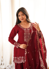Woman wearing a maroon traditional outfit with intricate designs indoors.