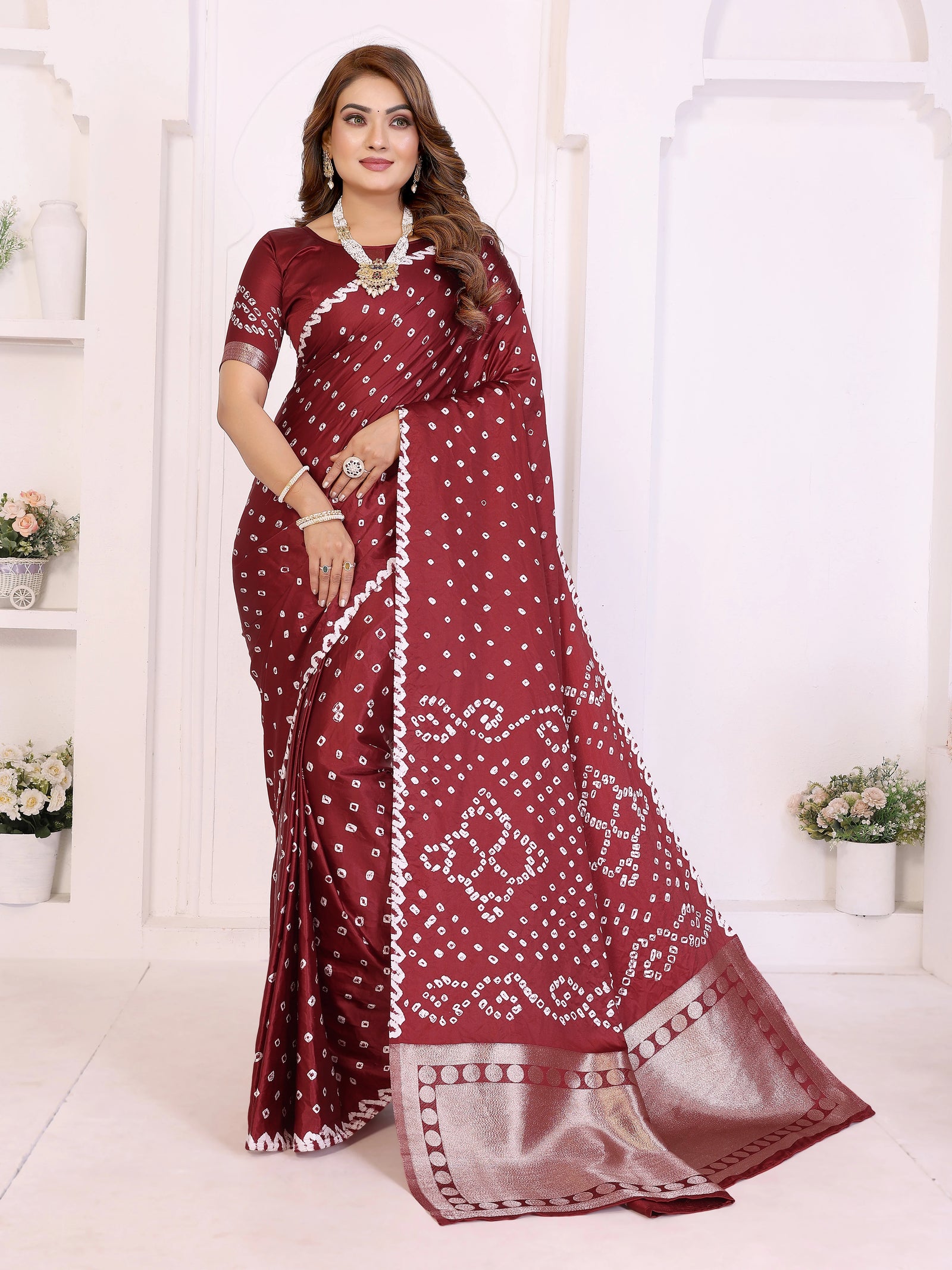 Woman wearing a maroon saree with white patterns in a white room.