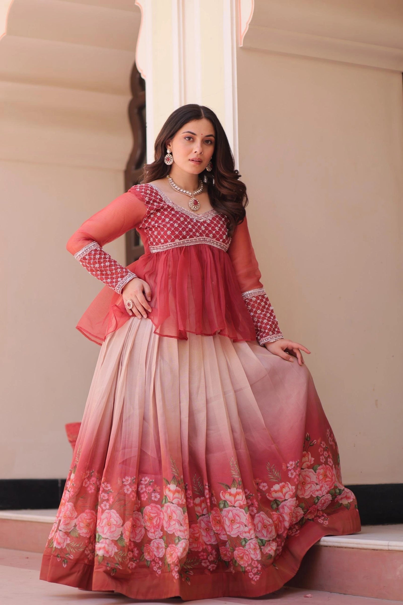 Woman wearing a red and pink traditional outfit with floral patterns indoors.