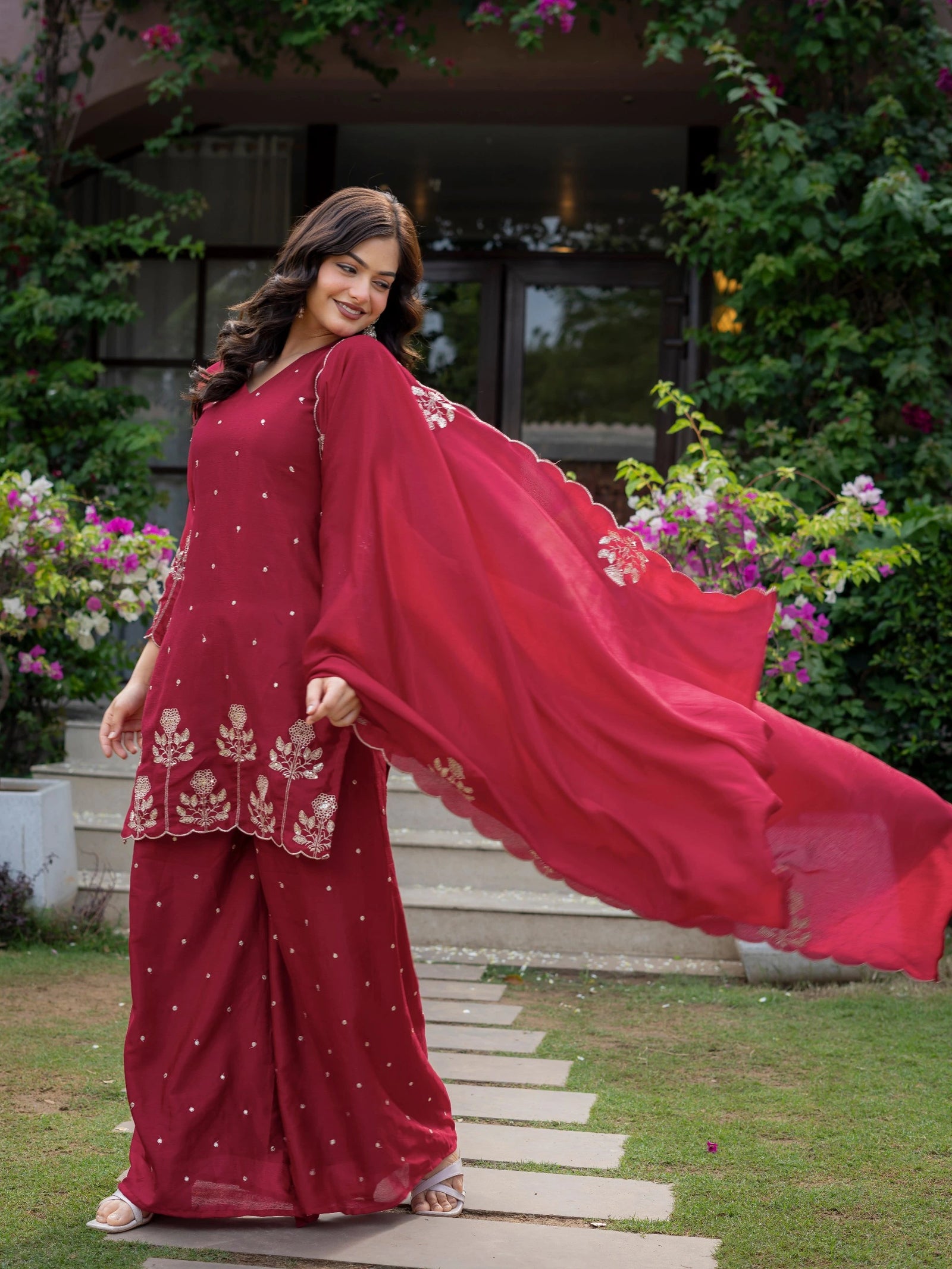 Woman in a red traditional outfit with a flowing dupatta standing outdoors.