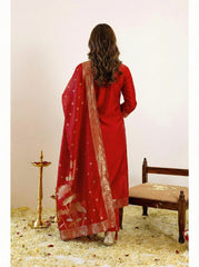 Woman wearing a red traditional outfit with a matching dupatta, standing in a decorated room.
