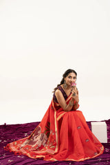Woman in a red saree sitting on a purple fabric with a white background
