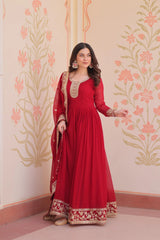 Woman wearing a red traditional outfit with gold embroidery against a floral wall.
