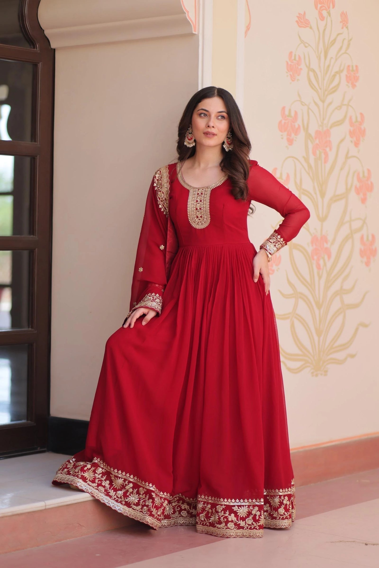 Woman wearing a red traditional outfit with gold embroidery in a decorated room.