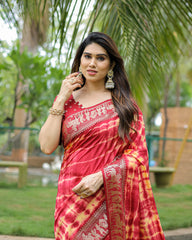 Woman in a red saree with white patterns standing outdoors with greenery in the background