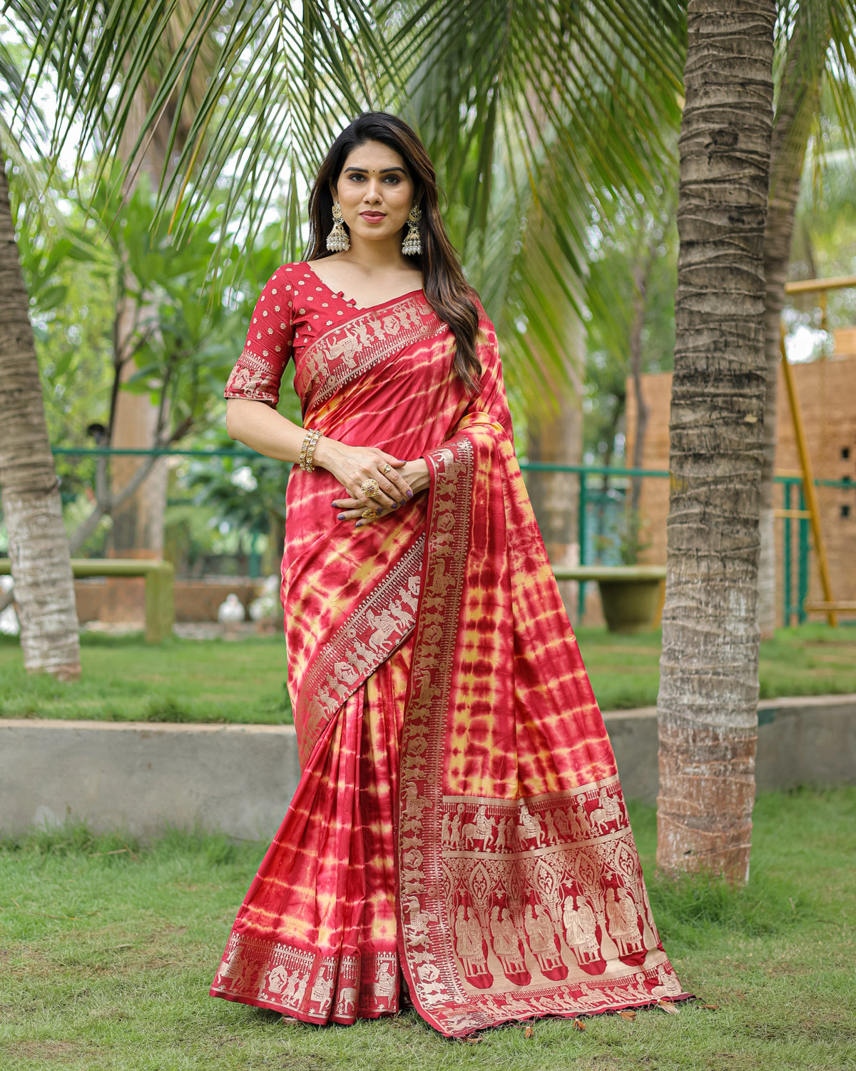 Woman in a red and white saree standing outdoors with palm trees in the background