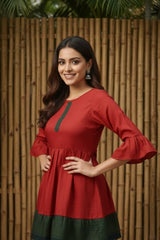 Woman wearing a red dress with green accents against a wooden fence background