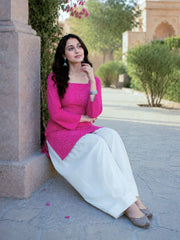 Woman in pink top and white pants sitting on a stone ledge outdoors.