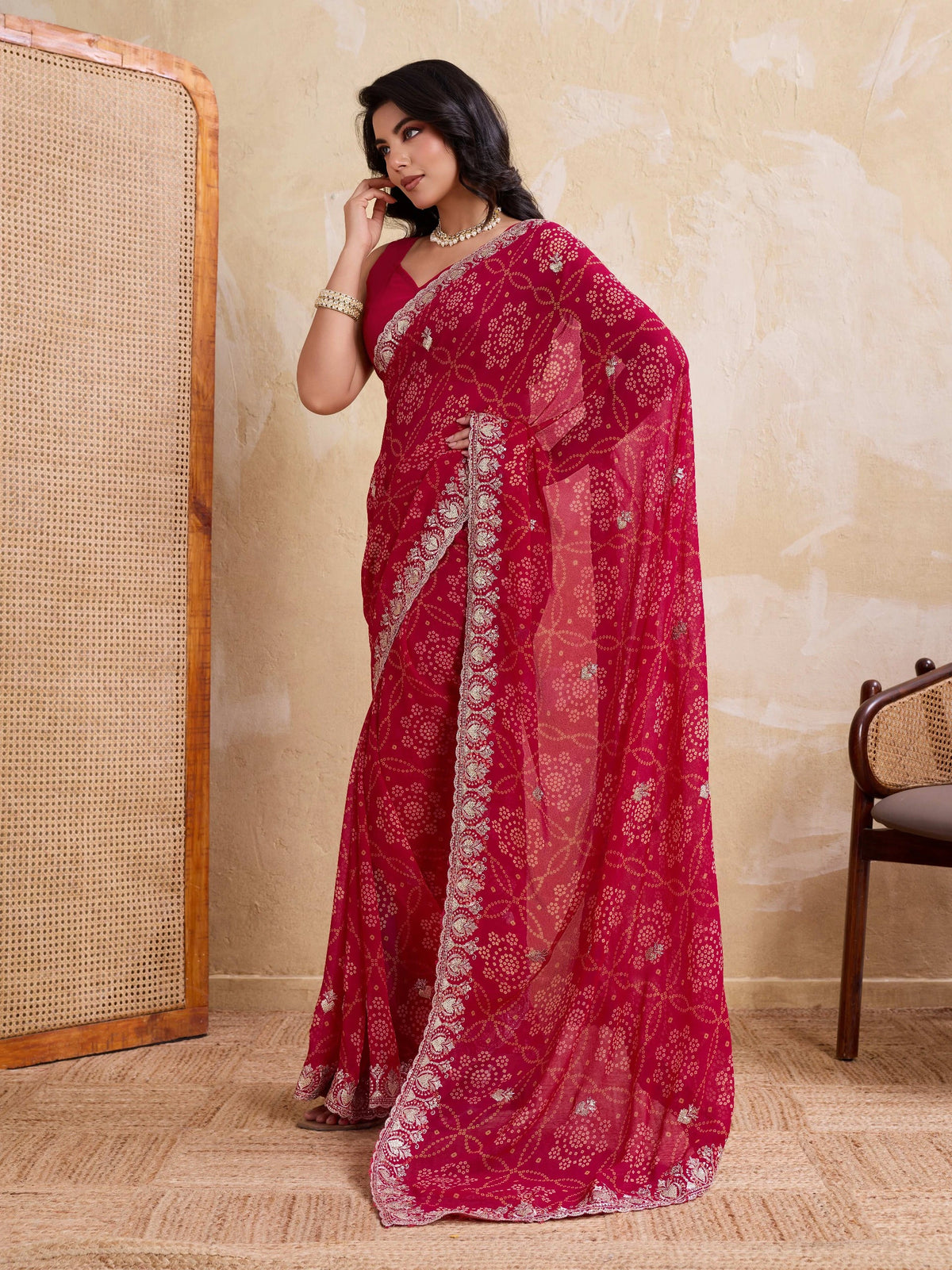 Woman wearing a red saree with white patterns against a beige wall.