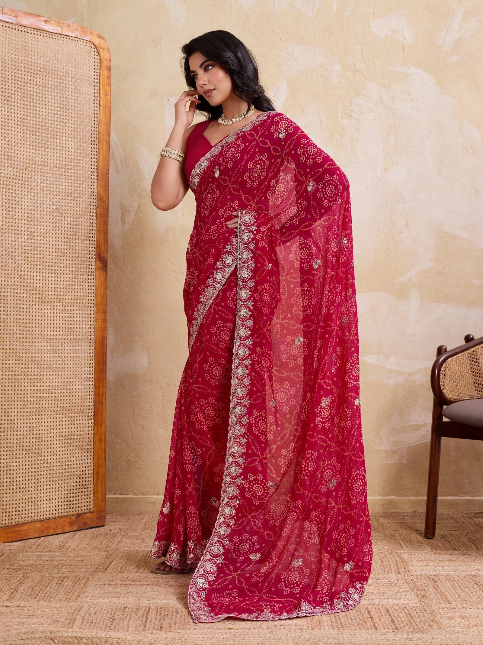 Woman wearing a red saree with white patterns against a beige wall.