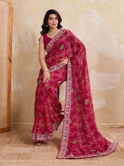 Woman wearing a red saree with intricate patterns against a beige wall.